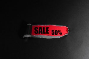 Svart papper med ett rivet hål som avslöjar texten SALE 50 procent på röd bakgrund.