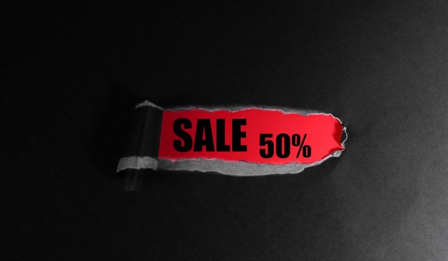 Svart papper med ett rivet hål som avslöjar texten SALE 50 procent på röd bakgrund.