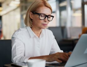 Kvinna med glasögon skriver på en laptop på ett kafé