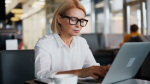 Kvinna med glasögon skriver på en laptop på ett kafé