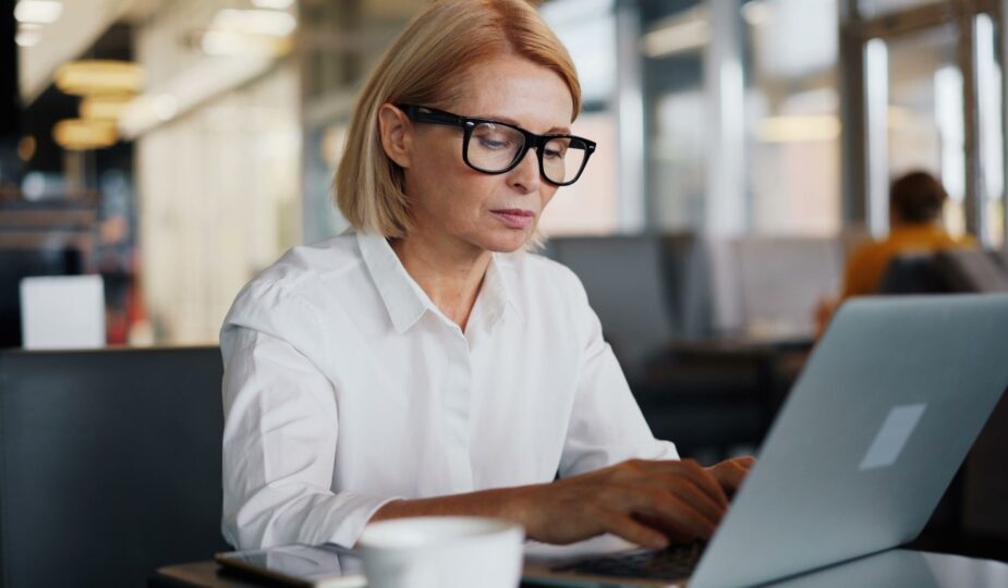 Kvinna med glasögon skriver på en laptop på ett kafé